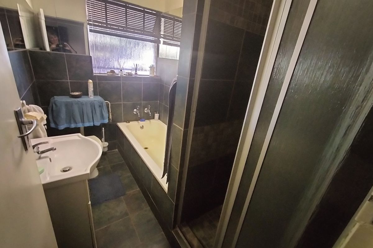 A functional bathroom featuring a tiled shower enclosure, a pedestal sink, and a built-in bathtub with dark wall tiling.