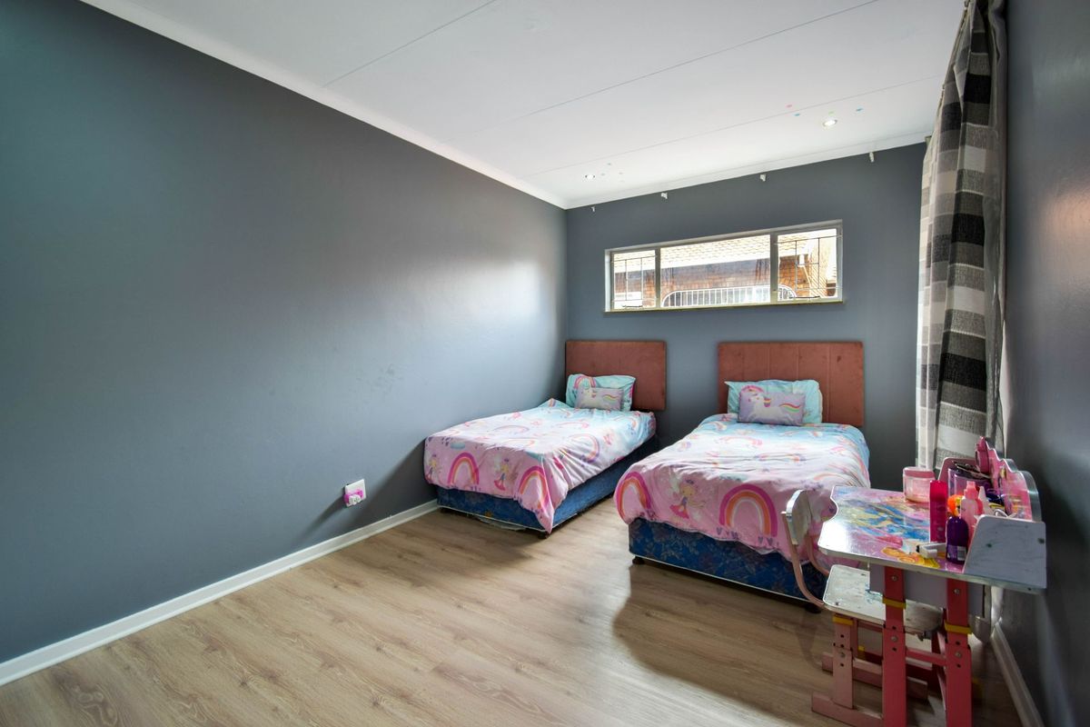 A well-lit bedroom featuring modern laminate flooring, dark grey painted walls, and a horizontal window providing natural light.