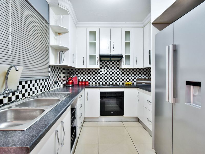 A functional kitchen featuring white cabinetry, black and white checkered backsplash, dark countertops, and integrated appliances including an oven and extractor fan.