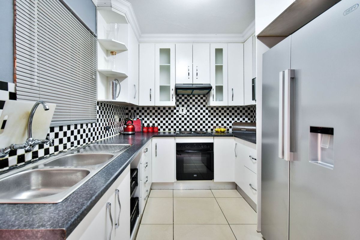 A functional kitchen featuring white cabinetry, black and white checkered backsplash, dark countertops, and integrated appliances including an oven and extractor fan.