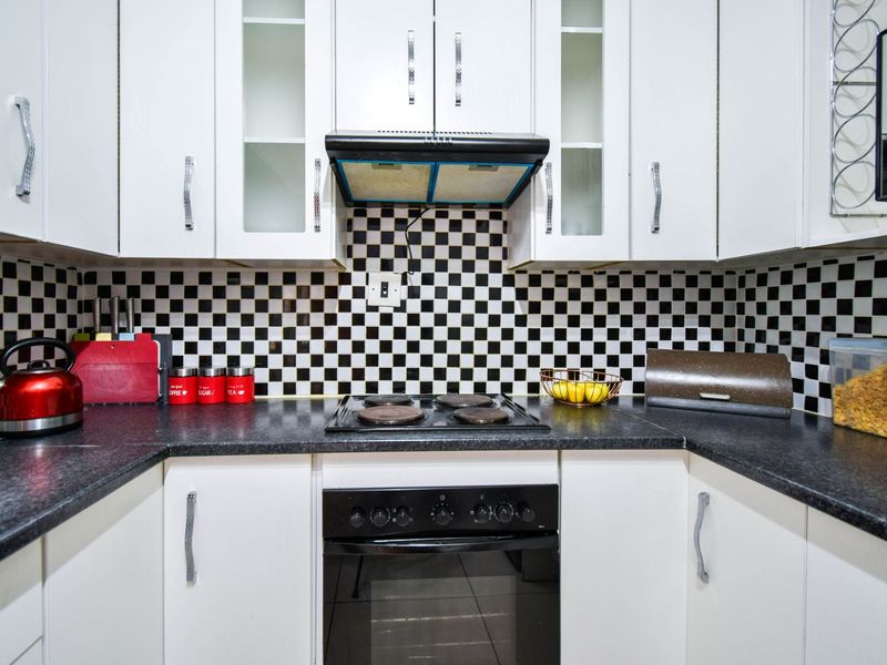 A compact kitchen featuring white cabinetry, black granite countertops, and a distinctive checkerboard tile backsplash with integrated oven and hob.