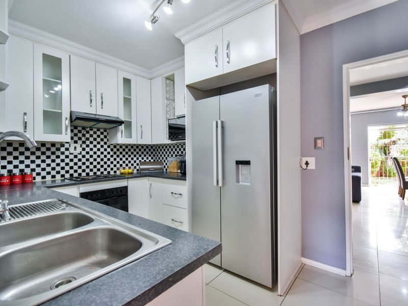 A well-maintained kitchen featuring white cabinetry, a checkered backsplash, built-in oven and hob, and a double stainless steel sink with laminate countertops.