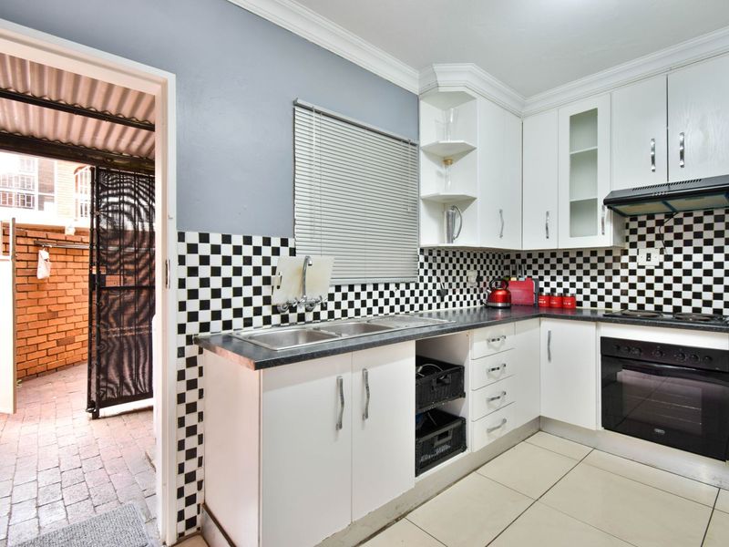 A functional kitchen featuring white cabinetry, a black and white checkered backsplash, built-in oven, extractor fan, and direct access to an outdoor courtyard area.