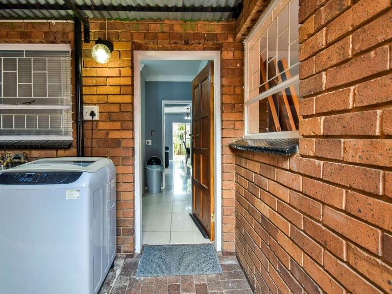 A functional outdoor laundry area featuring exposed brick walls, tiled flooring, and direct access into the home's interior hallway.
