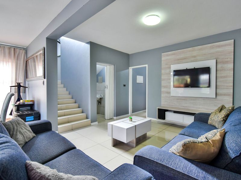 A well-maintained living room featuring tiled flooring, a modern built-in media wall, and an integrated staircase leading to the upper level.