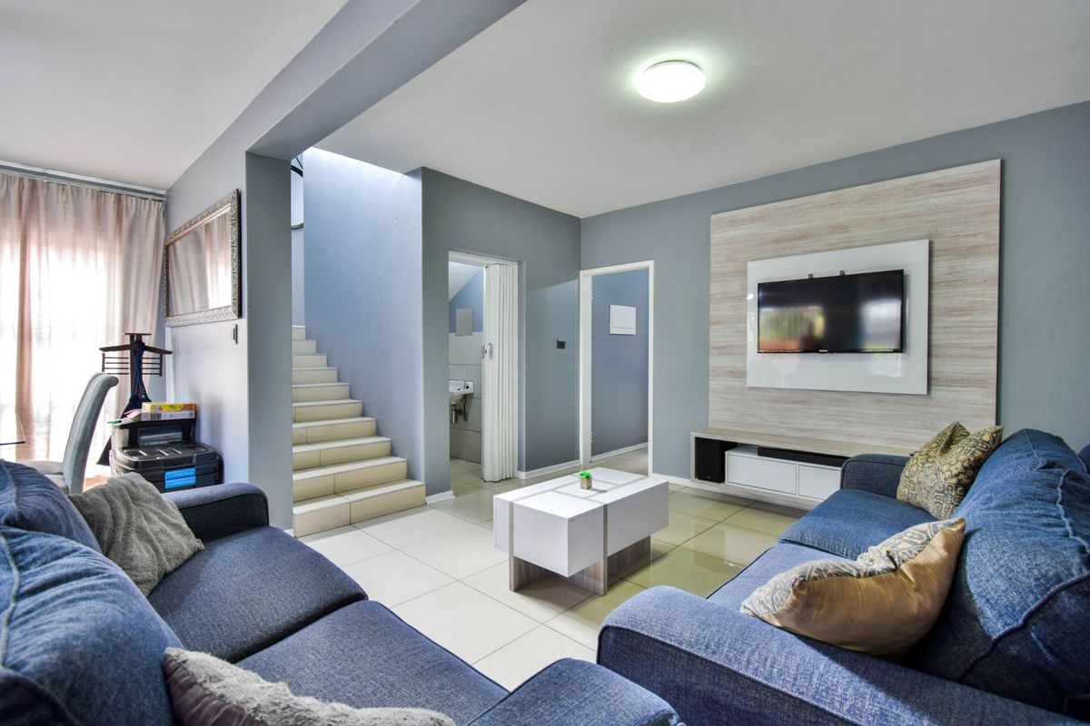 A well-maintained living room featuring tiled flooring, a modern built-in media wall, and an integrated staircase leading to the upper level.