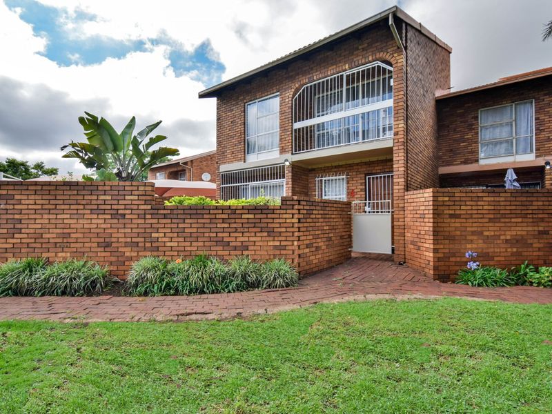 Front view of a double-story face brick townhouse featuring a private garden, paved walkway, and secure gated entrance with a balcony.