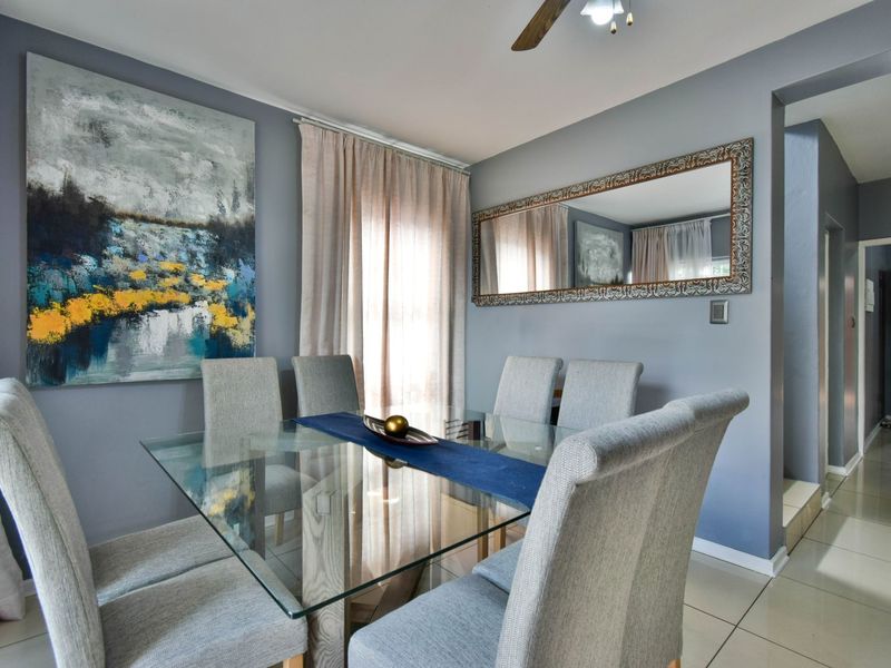 A well-maintained dining room featuring neutral tiled flooring, a ceiling fan, and direct access to an adjacent hallway.