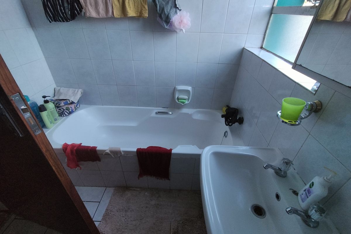 A functional bathroom featuring a standard bathtub, a wall-mounted washbasin, and tiled finishes throughout, providing a practical space for daily use.