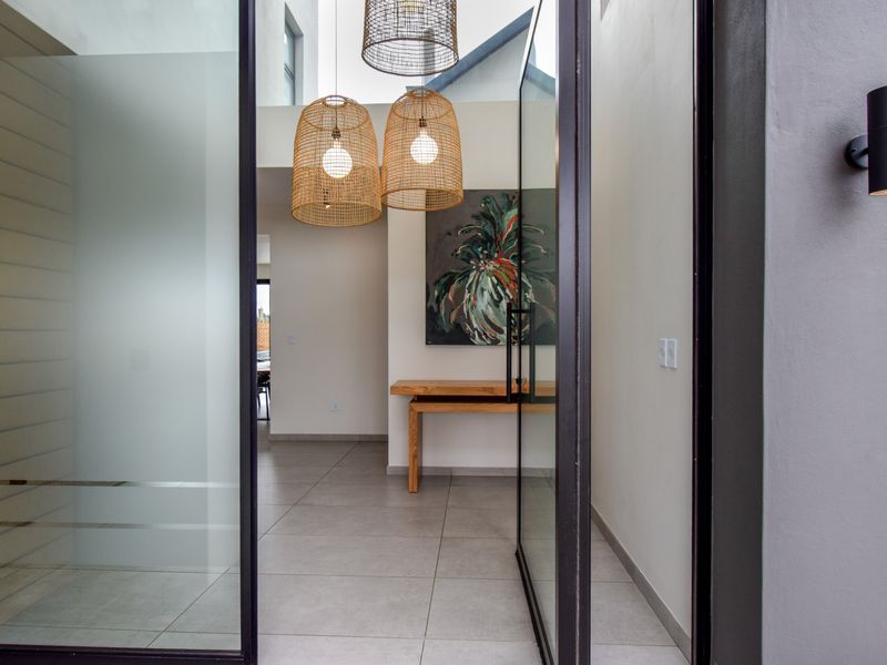 Modern entrance hall featuring large format floor tiles, double volume ceiling height, and a contemporary glass pivot door.