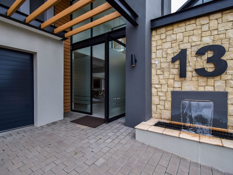 Modern front entrance featuring stone cladding, a built-in water feature, timber pergola detailing, and a sleek glass entry door with adjacent garage access.