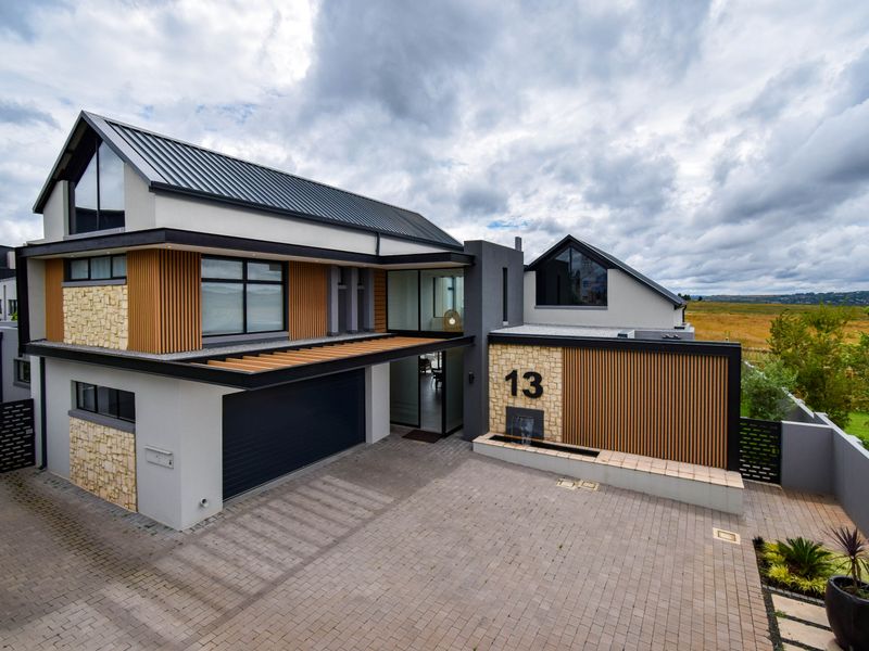Modern architectural home featuring a striking combination of stone, timber slats, and metal roofing with a paved driveway and integrated water feature.