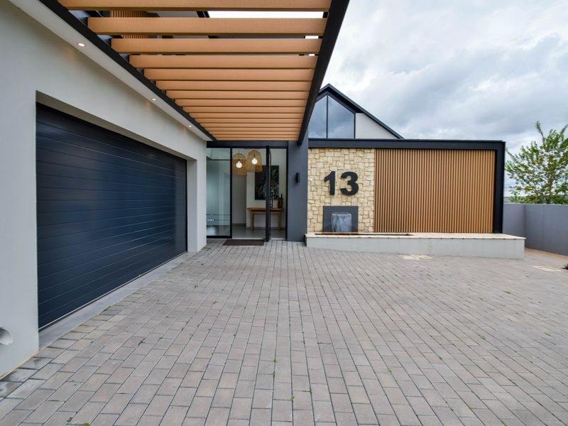 Modern front facade featuring a paved driveway, timber pergola, stone and timber cladding, and a built-in water feature at the entrance.