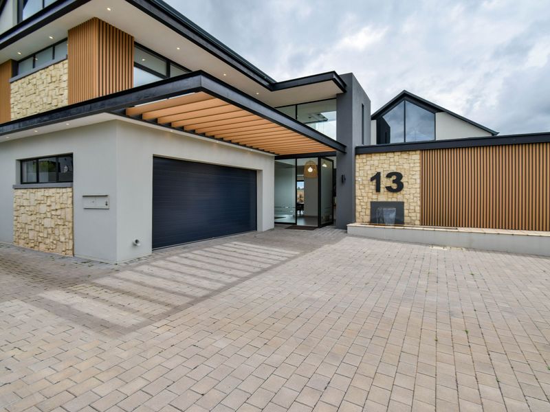 Modern architectural front facade featuring stone and timber cladding, a paved driveway, automated garage, and a contemporary entrance with a built-in water feature.