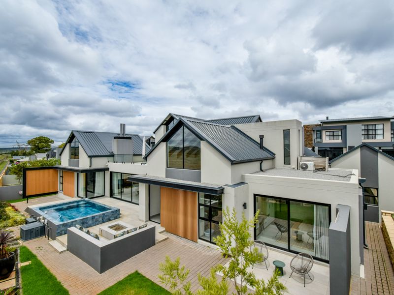 Modern rear exterior view featuring a swimming pool, built-in fire pit, paved patio area, and contemporary architectural design with metal roofing and timber accents.