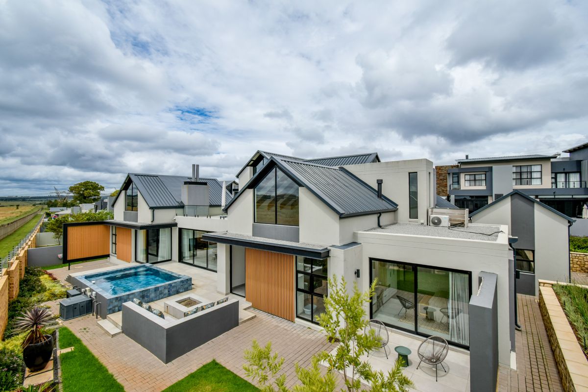 Modern rear exterior view featuring a swimming pool, built-in fire pit, paved patio area, and contemporary architectural design with metal roofing and timber accents.