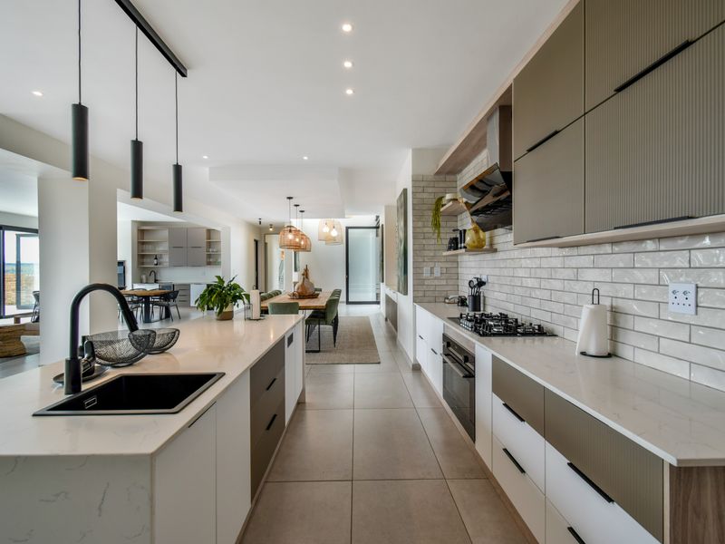 Modern open-plan kitchen featuring a large island, quartz countertops, high-end built-in appliances, and stylish subway tile backsplash, flowing into the dining area.