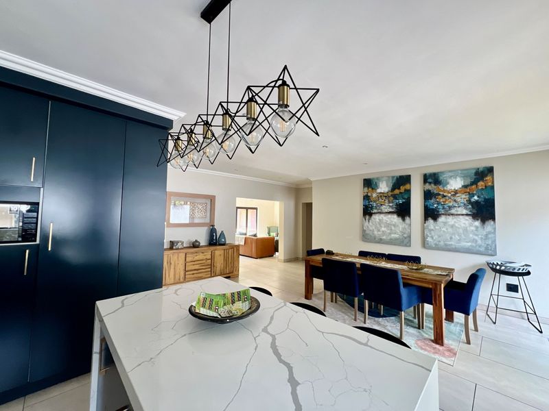 Modern open-plan living and dining area featuring a large kitchen island with stone countertop, sleek dark cabinetry, and contemporary pendant lighting.