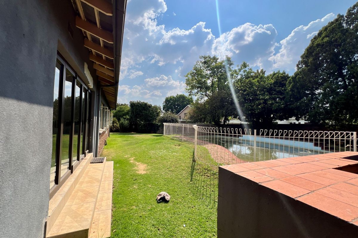 Rear garden area featuring a swimming pool with safety fencing, a tiled patio, and a brick built-in braai structure adjacent to the house.