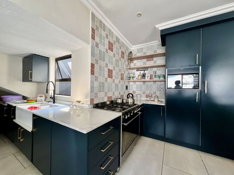 Modern kitchen featuring dark cabinetry, quartz countertops, a farmhouse sink, gas cooktop, and decorative tiled backsplash with integrated lighting.