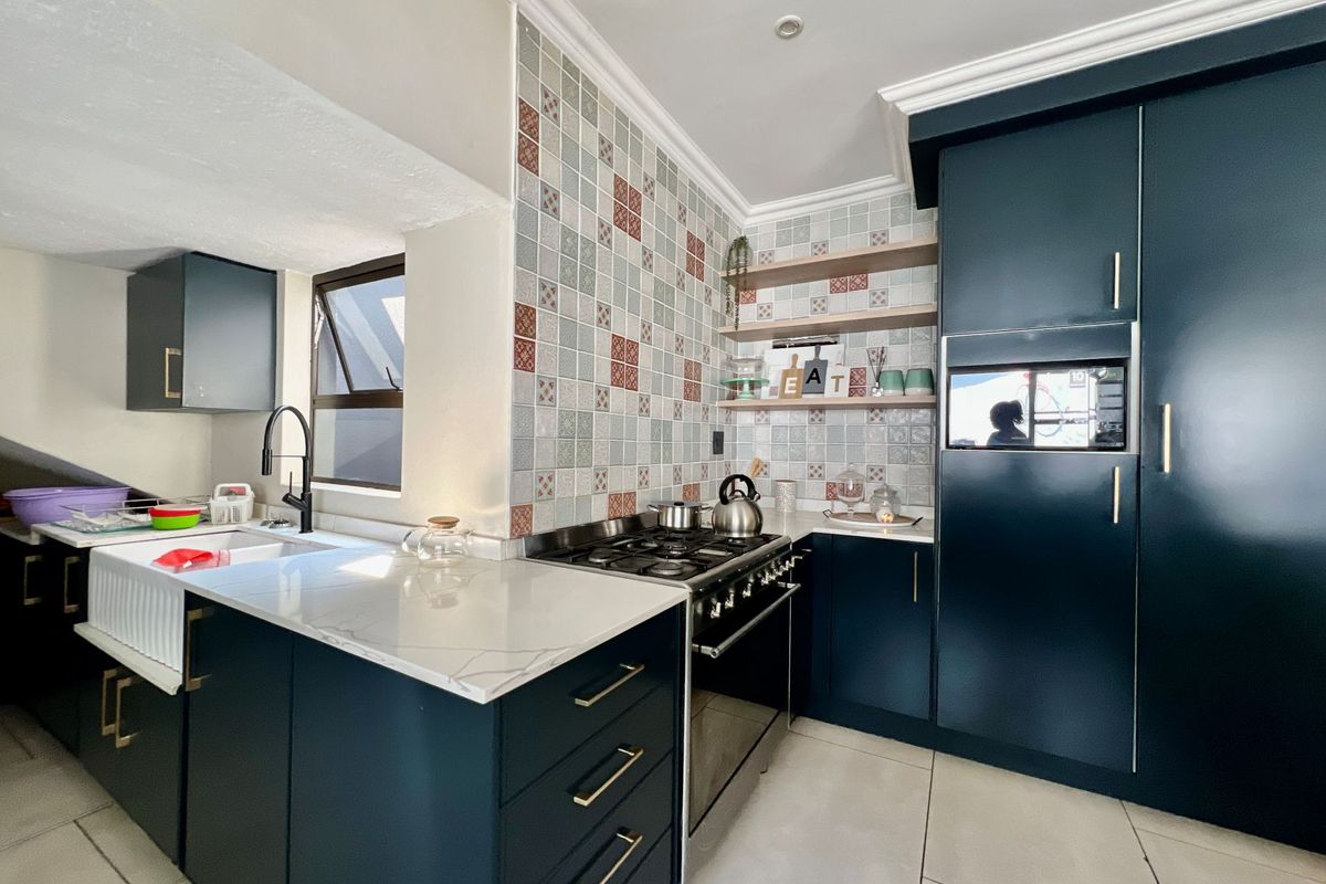 Modern kitchen featuring dark cabinetry, quartz countertops, a farmhouse sink, gas cooktop, and decorative tiled backsplash with integrated lighting.