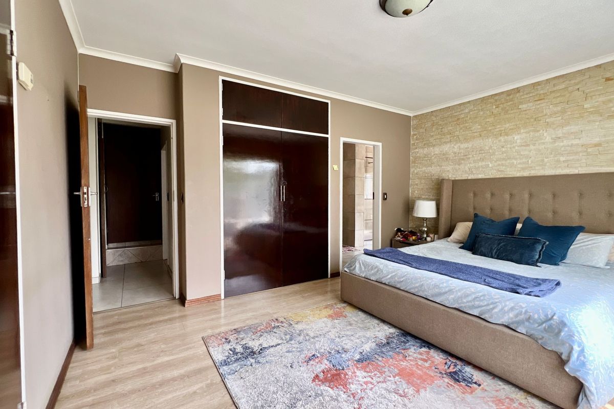 Spacious bedroom featuring laminate flooring, a stone-clad feature wall, and built-in dark wood cupboards with direct access to an adjoining room.