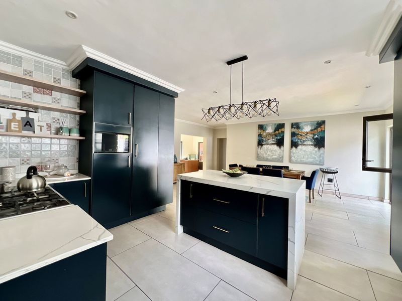 Modern open-plan kitchen featuring dark cabinetry, stone countertops, a central island, and integrated appliances, flowing seamlessly into the dining area.