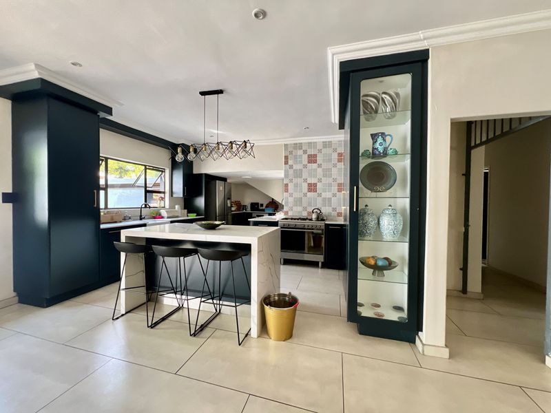 Modern kitchen featuring a central island with stone countertops, dark cabinetry, gas stove, tiled backsplash, and integrated glass display shelving.
