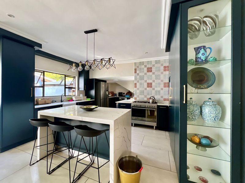 Modern kitchen featuring a central stone-topped island, dark cabinetry, gas stove, and a built-in glass display cabinet with tiled flooring throughout.