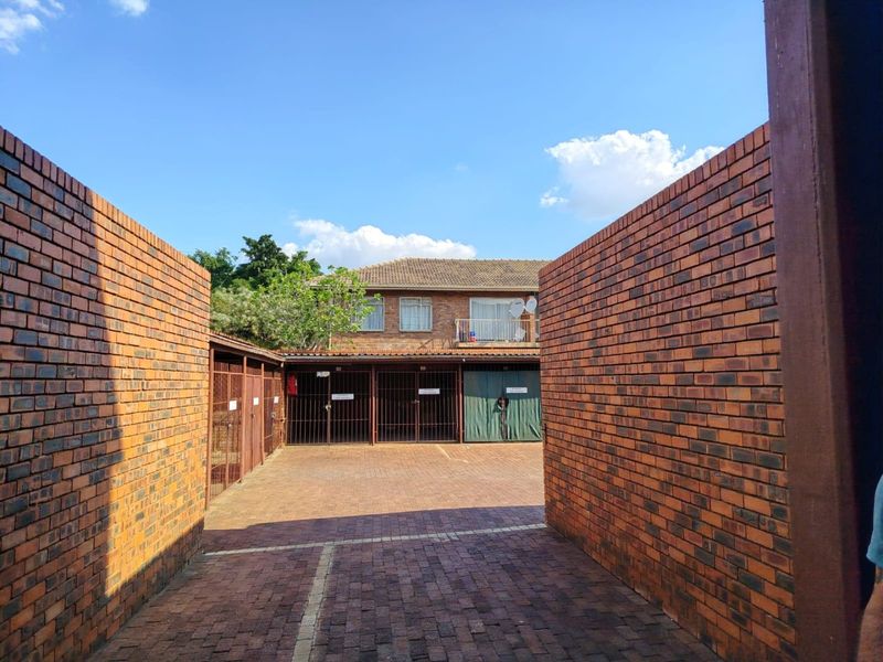 A secure outdoor parking area featuring brick paving, enclosed by brick boundary walls and metal security gates.