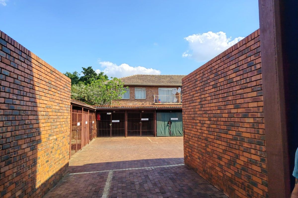 A secure outdoor parking area featuring brick paving, enclosed by brick boundary walls and metal security gates.
