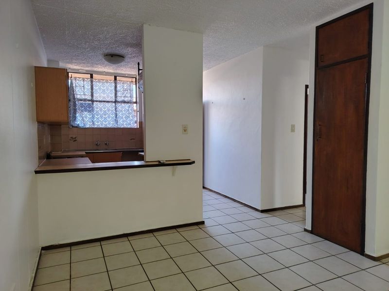 An open-plan living and kitchen area featuring tiled flooring, a breakfast bar, and built-in storage, offering a blank canvas for renovation.
