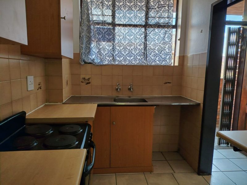A compact kitchen featuring dated cabinetry, a stainless steel sink, tiled backsplash, and an electric stove, offering potential for modernization.