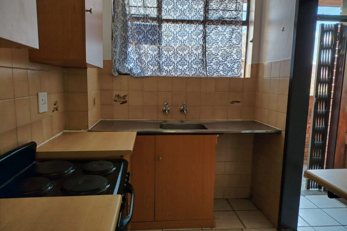 A compact kitchen featuring dated cabinetry, a stainless steel sink, tiled backsplash, and an electric stove, offering potential for modernization.
