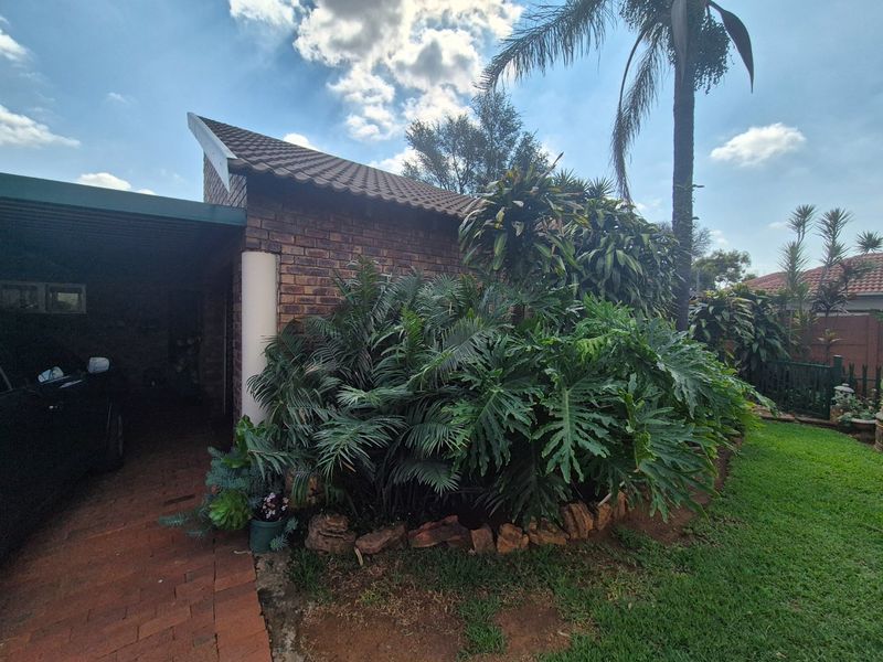 Front view of a brick house featuring a tiled roof, a covered carport, and a well-established garden with stone edging.