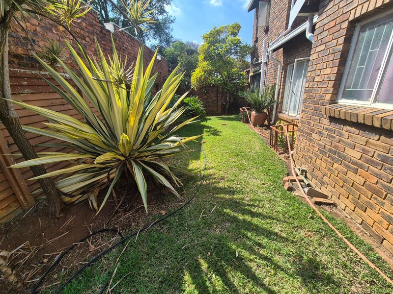 A side garden area featuring a face brick exterior wall, lawn, and established landscaping along the boundary wall.