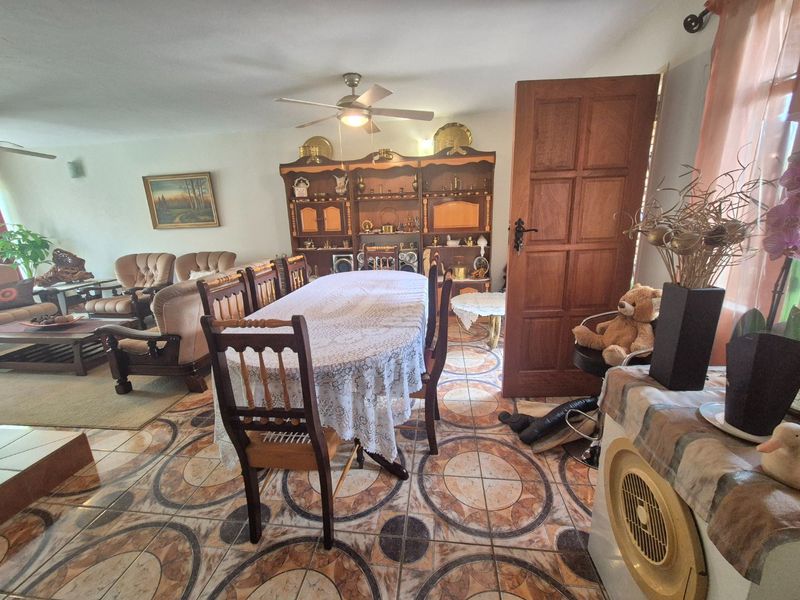 Open plan living and dining area featuring patterned ceramic tile flooring, a ceiling fan, and a traditional wooden door.