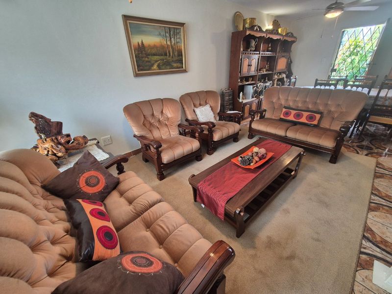 A spacious living room featuring neutral carpeting, a ceiling fan, and access to an outdoor area through a security gate.