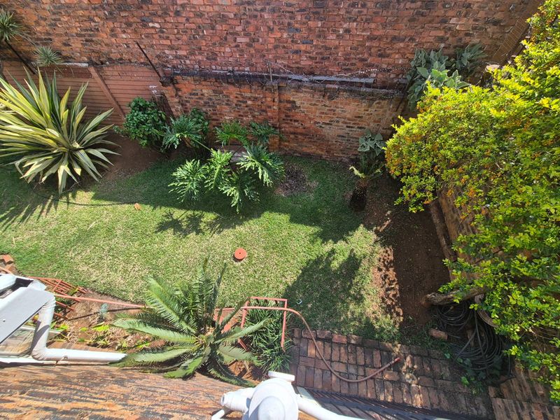 An elevated view of a private rear garden featuring a lawn, established greenery, and traditional brick boundary walls.