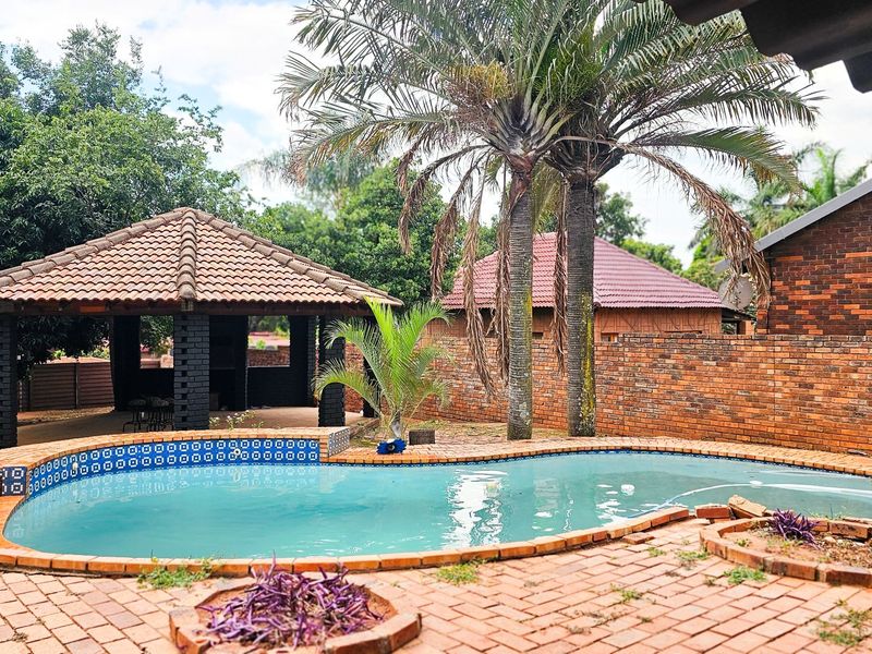 Outdoor pool area featuring a swimming pool, brick paving, and a thatched gazebo, set within a private garden with brick boundary walls.