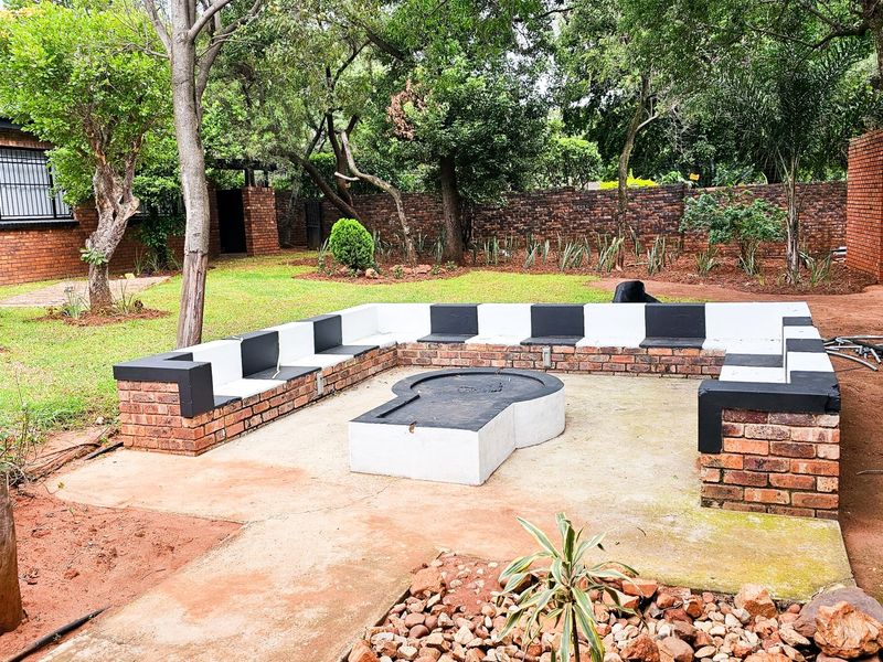 Outdoor entertainment area featuring a built-in brick fire pit and integrated bench seating, set within a landscaped garden with mature trees.