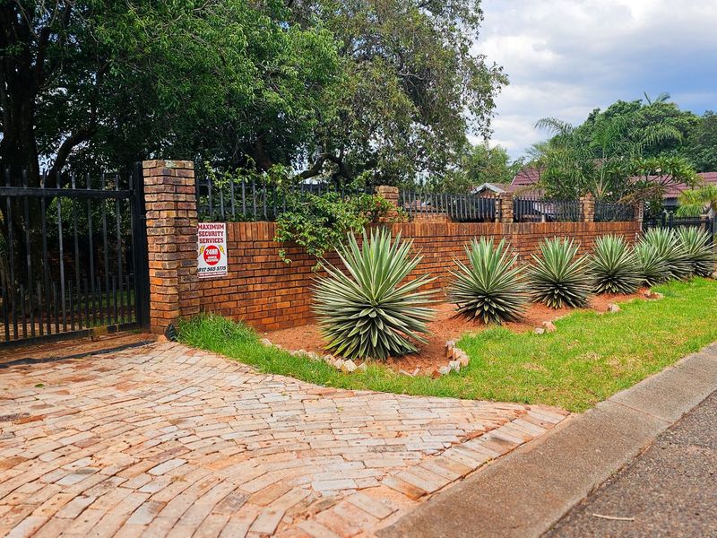 Street view of the property featuring a brick boundary wall, metal security gate, and a paved driveway entrance.