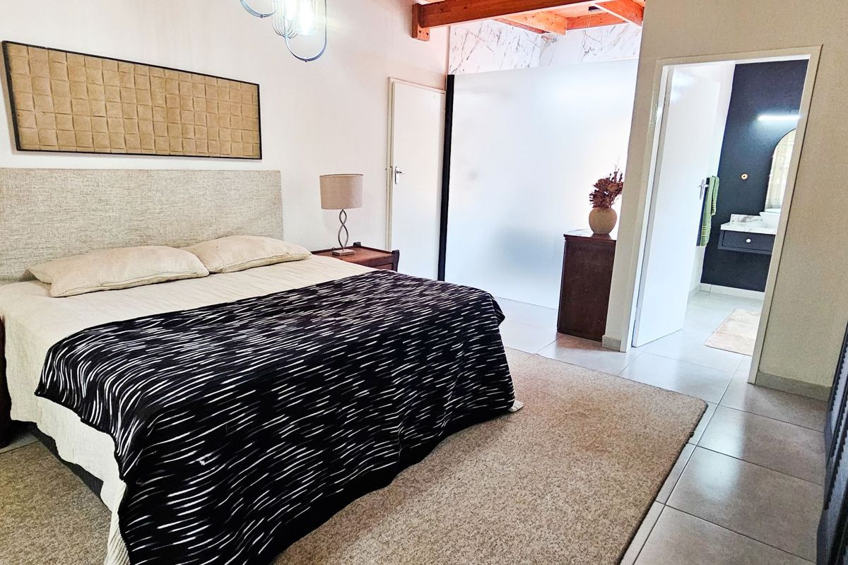 Spacious bedroom featuring exposed timber ceiling beams, tiled flooring, and a modern frosted glass partition leading to an en-suite bathroom.