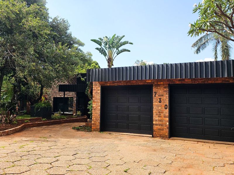 Front view of a residential property featuring a double garage with black doors, brick exterior, and a paved driveway set within a landscaped garden.