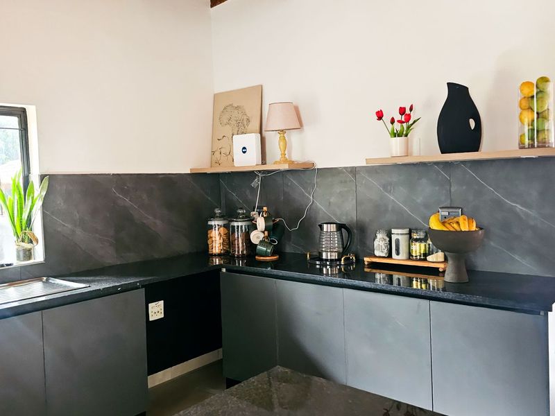 Modern kitchen featuring dark grey cabinetry, sleek stone countertops, a matching stone slab backsplash, and floating timber shelving for a contemporary aesthetic.