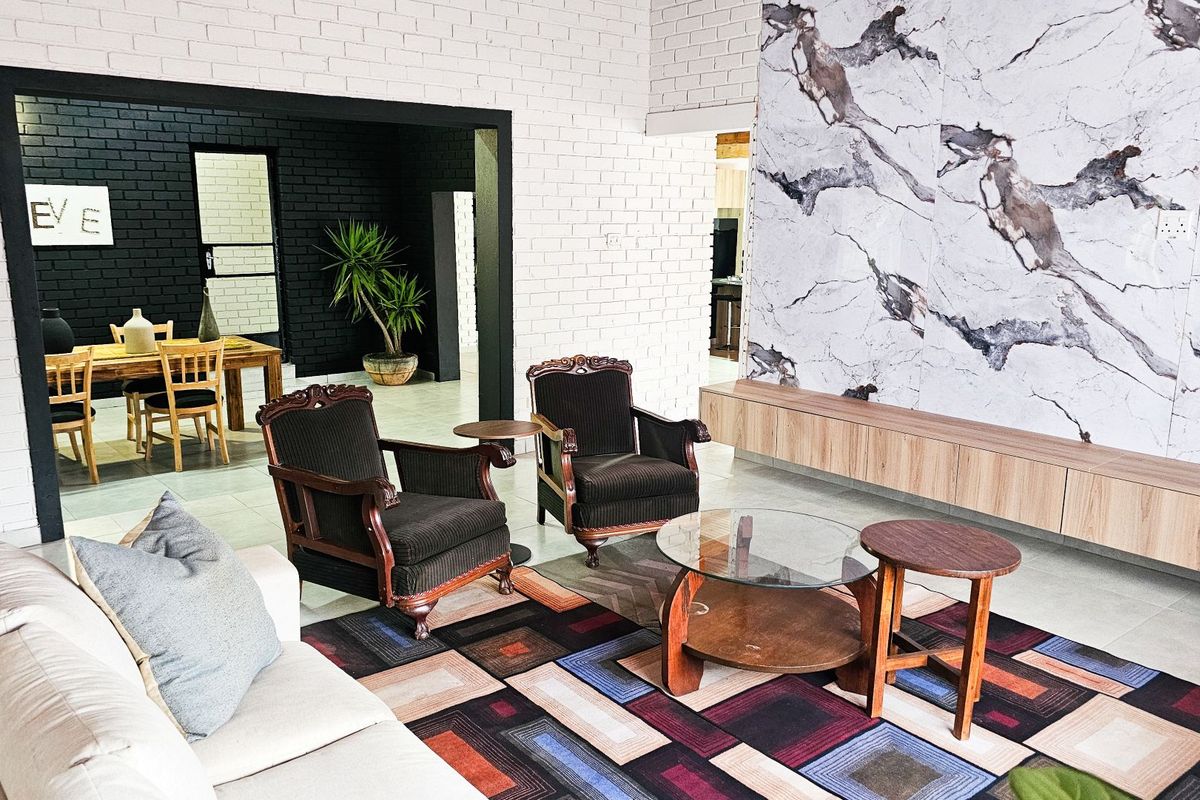 Spacious living room featuring a striking marble-look feature wall with integrated floating cabinetry, complemented by painted brick walls and neutral tiled flooring.
