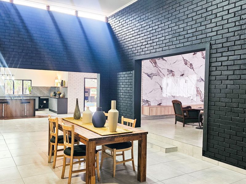 Spacious open-plan living and dining area featuring striking black exposed brick walls, high vaulted ceilings with clerestory windows, and modern tiled flooring.