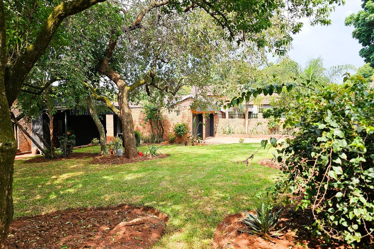 A spacious rear garden featuring a well-maintained lawn, mature trees, and a brick-faced building exterior.