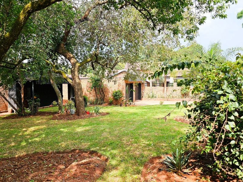 A spacious rear garden featuring a well-maintained lawn, mature trees, and a brick-faced building exterior.