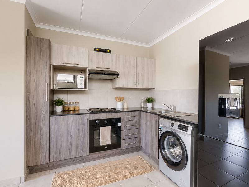 Modern kitchen featuring wood-grain cabinetry, integrated appliances, electric hob, oven, and a convenient built-in washing machine space.